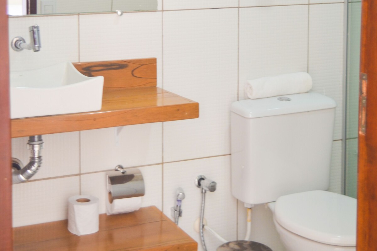A bathroom with a white sink, wooden countertop, toilet, and a trash can.