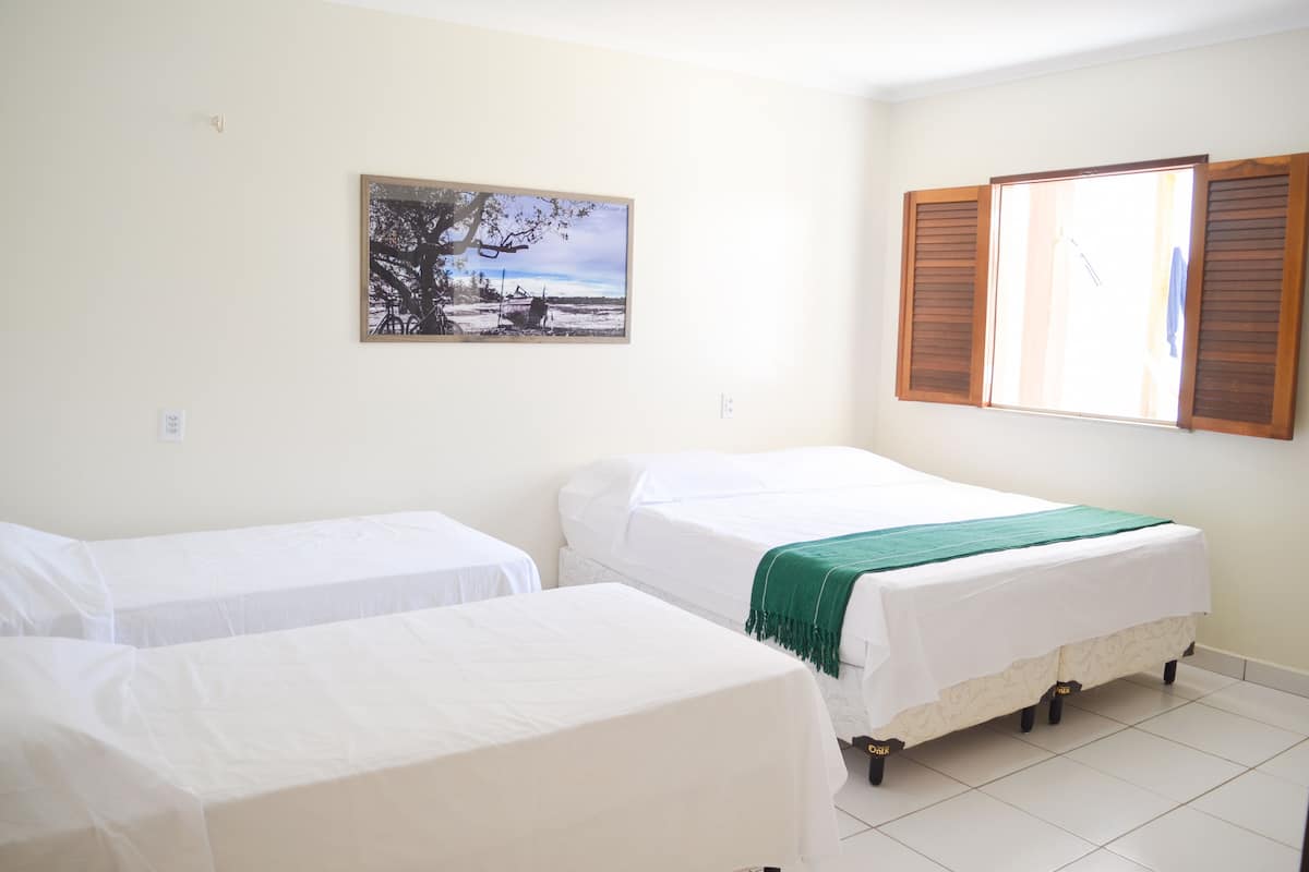 A room with two single beds, a framed picture on the wall, and a window with wooden shutters.
