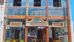 A two-story building with a wooden facade and large windows. The ground floor has a sign that reads "Boteco Vila Tutoria."