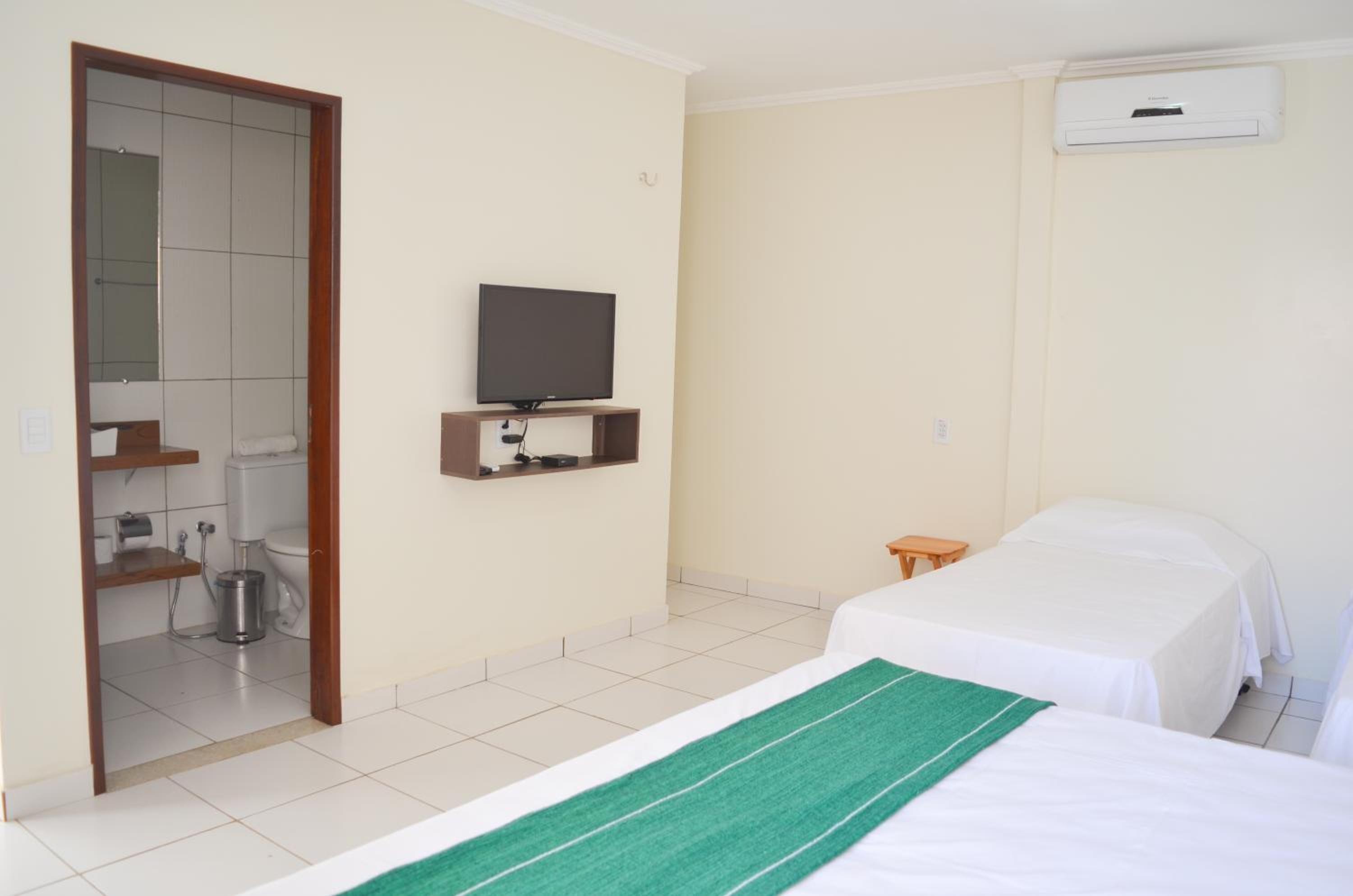 Een hotelkamer met een televisie, twee bedden, een klein tafeltje, een toilet en een douche.