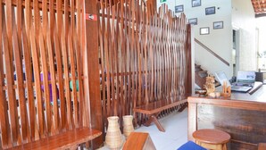 A reception area with a wooden partition, a bench, a laptop, and a small table with decorative items.