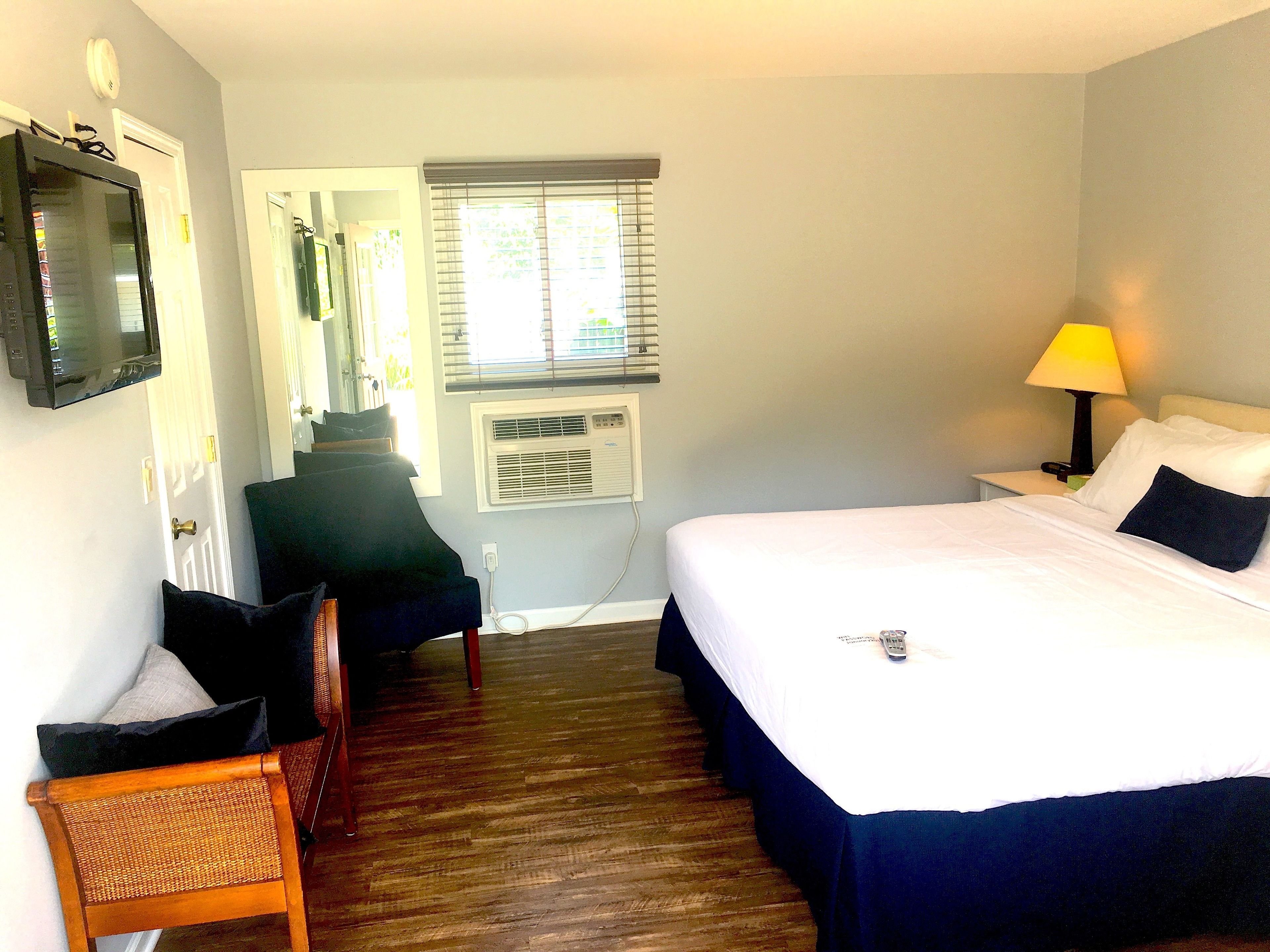 Une chambre d’hôtel avec un lit, une chaise, une télévision, une fenêtre avec des stores et une lampe.