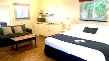 A hotel room with a bed, a sofa, a desk with a microwave, and a window with blinds.