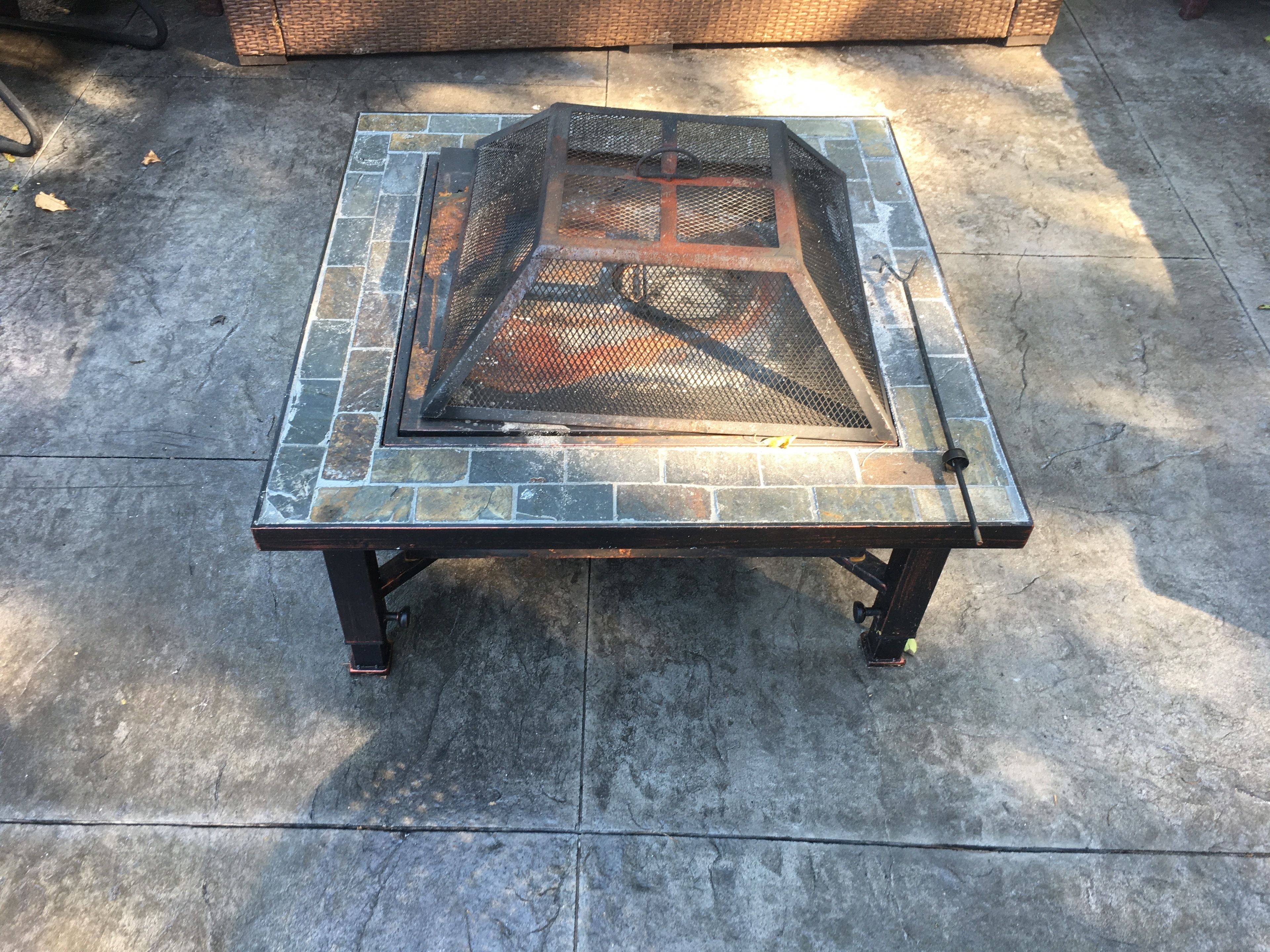 Ein quadratischer Tisch im Freien mit einem Grill auf der Tischplatte, auf einem mit Steinplatten belegten Boden.