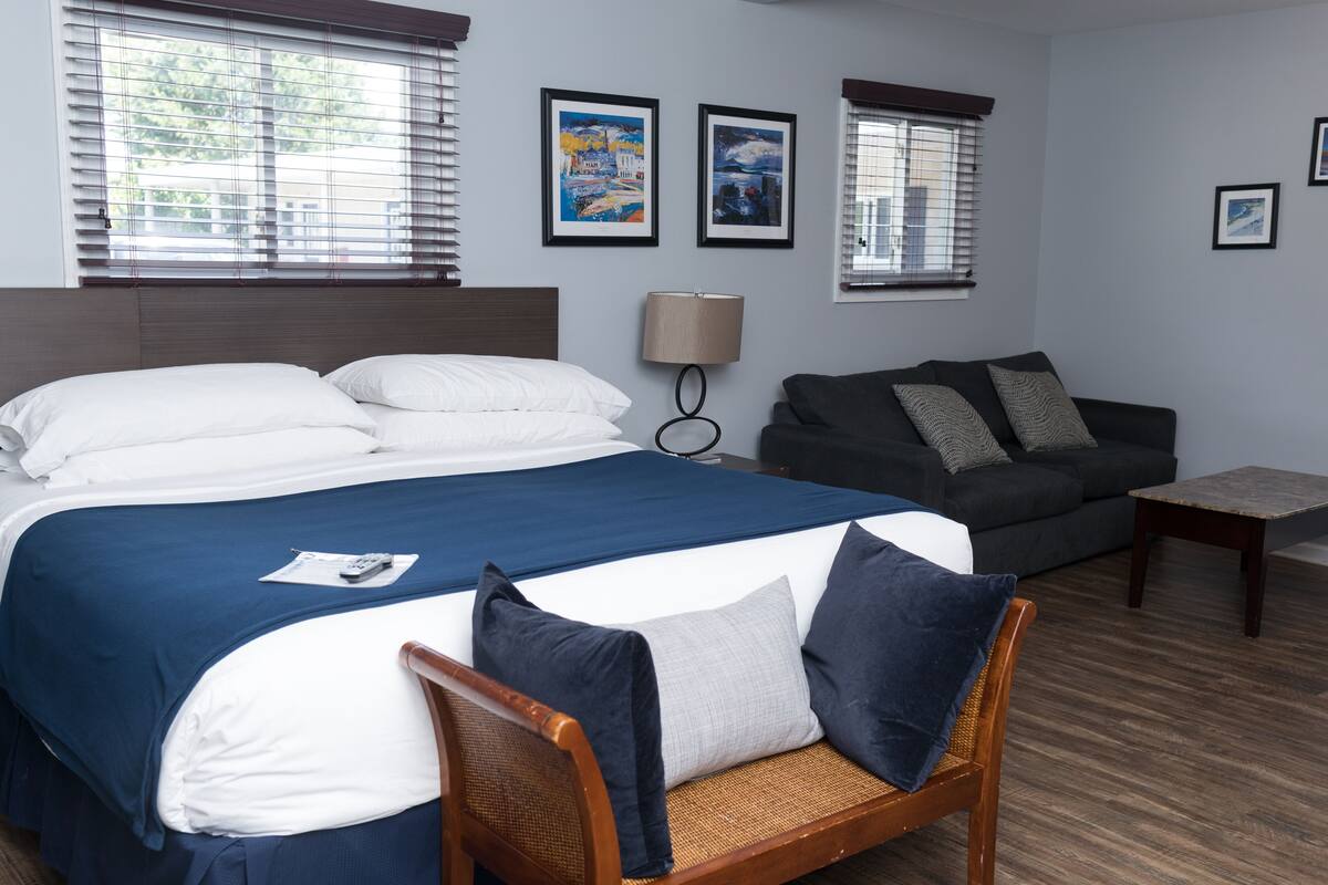 A hotel room with a large bed, a sofa, a small table, and artwork on the walls.