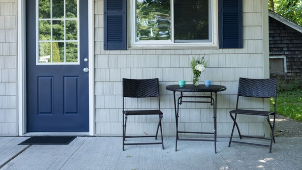 A house with a dark blue door, a window with shutters, and two chairs and a table outside.