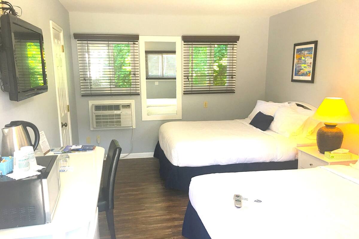 A hotel room with two beds, a desk, a chair, and a window with blinds.