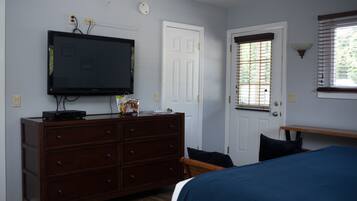 A bedroom with a TV mounted on the wall, a dresser, a door with a window, and a bedside table.