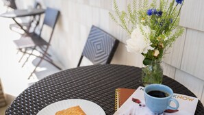 A round table with a black woven tablecloth, a white plate with a pastry, a blue coffee cup, a vase with flowers, and a magazine featuring a dog.