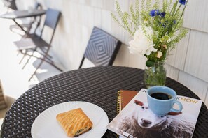 A round table with a black woven tablecloth, a white plate with a pastry, a blue coffee cup, a vase with flowers, and a magazine featuring a dog.
