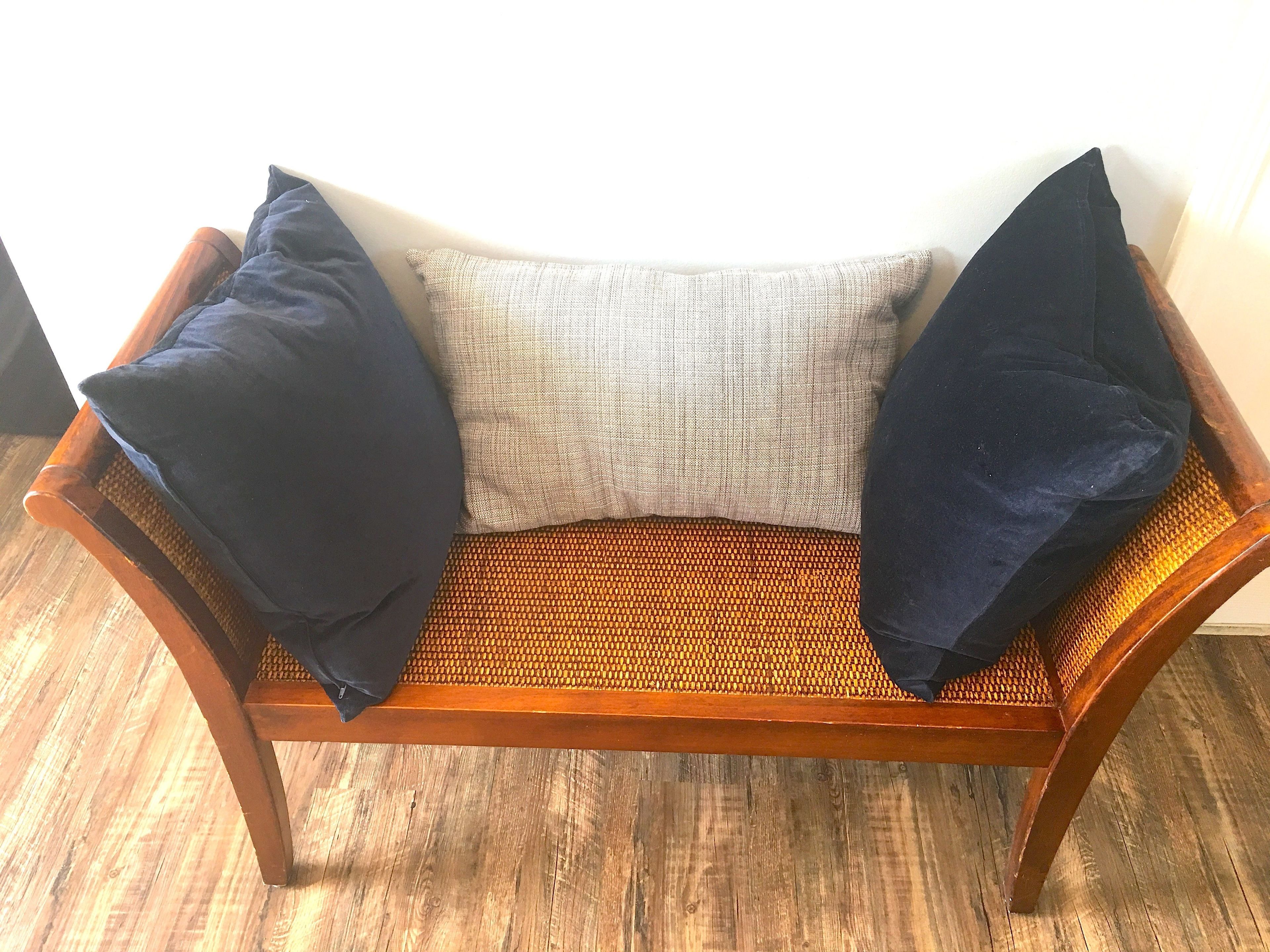 A wooden bench with a woven seat and backrest, featuring two dark blue cushions and a light grey cushion.