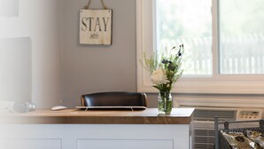 Una recepción con un jarrón de flores, un cartel que dice "STAY awhile" y una ventana con persianas.