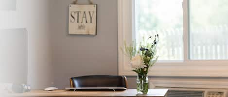 A reception desk with a vase of flowers, a sign that says "STAY awhile", and a window with blinds.