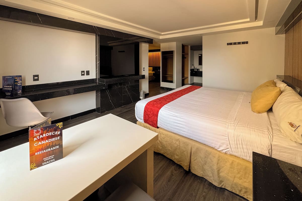A hotel room with a bed, a desk, a TV, a mirror, and a sign for a restaurant.