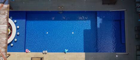 Ein rechteckiger Swimmingpool mit blauer Innenseite, umgeben von einer gefliesten Terrasse und einer niedrigen Mauer.