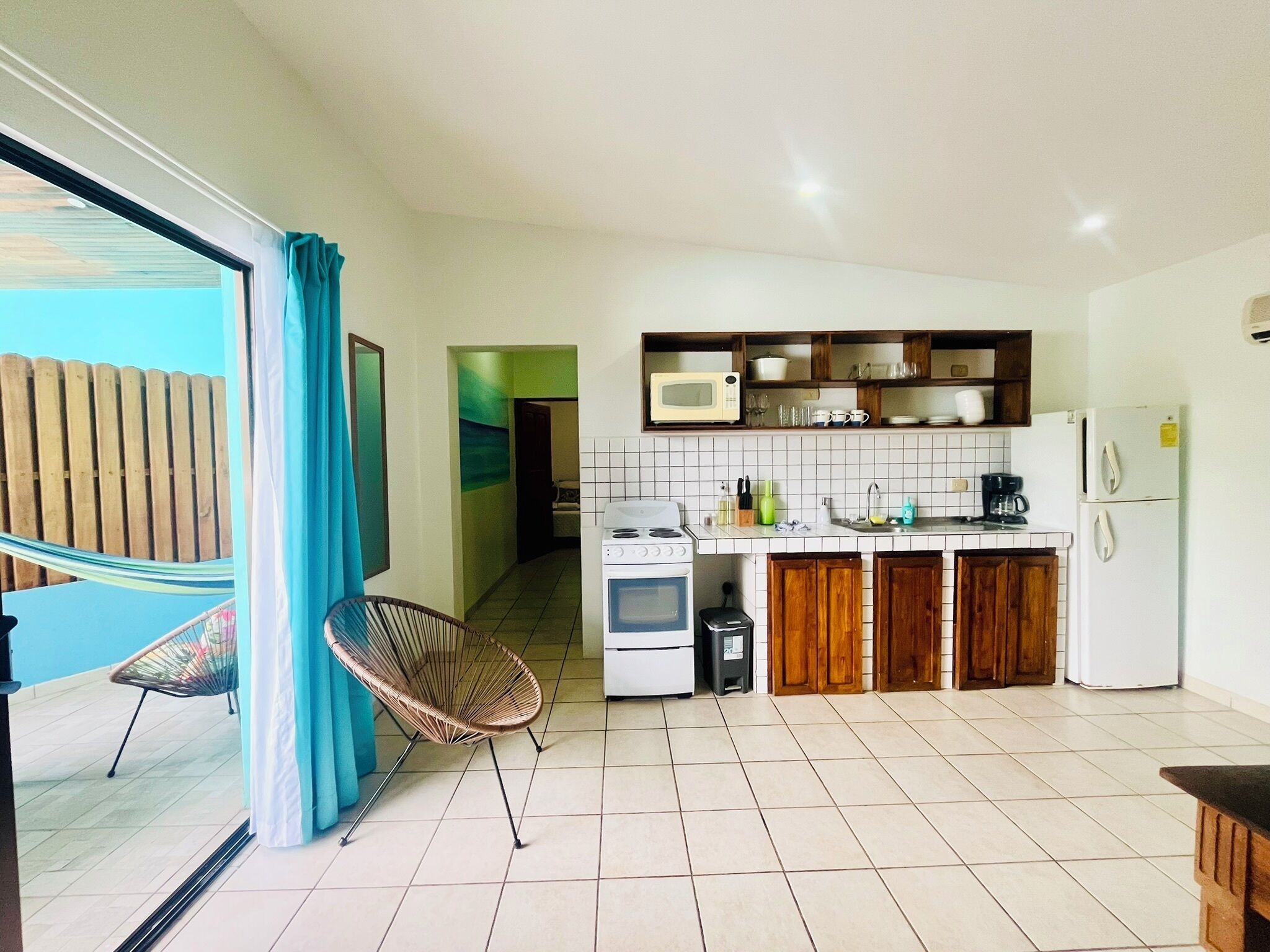 A kitchen with a stove, microwave, and refrigerator. There is a chair and a hammock in the adjacent area.
