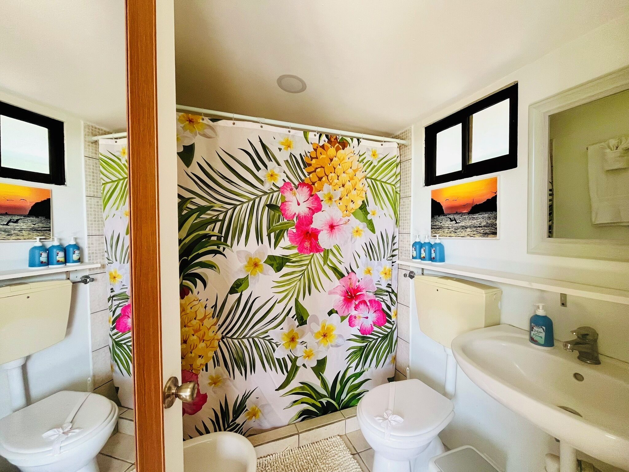 A bathroom with two white sinks, a toilet, and a shower curtain with a tropical floral pattern.