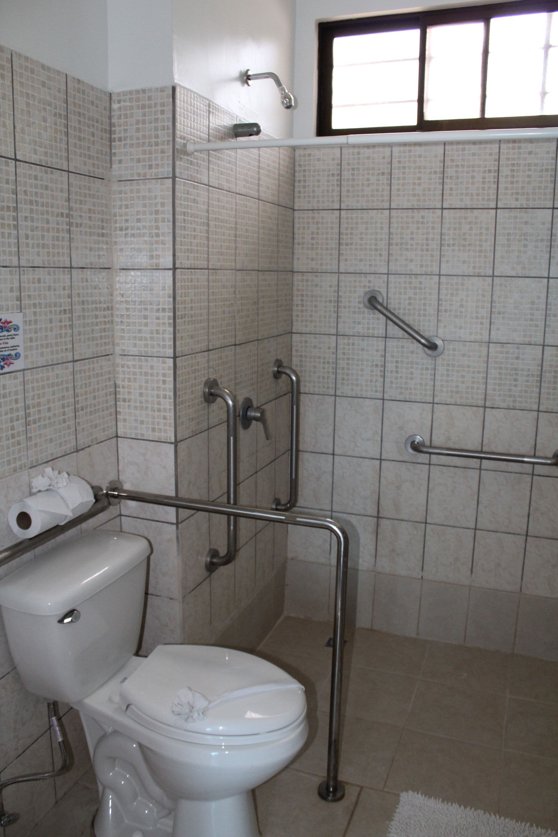 Une salle de bain équipée de toilettes, de barres d’appui et d’une fenêtre.