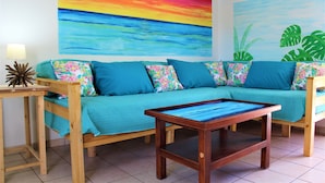 Una habitación con un sofá color turquesa, una mesa de centro de madera y un mural con un atardecer colorido en la pared.