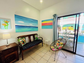Una habitación con un banco de madera, una silla y vistas a un espacio exterior con mesas y sillas a través de un ventanal.