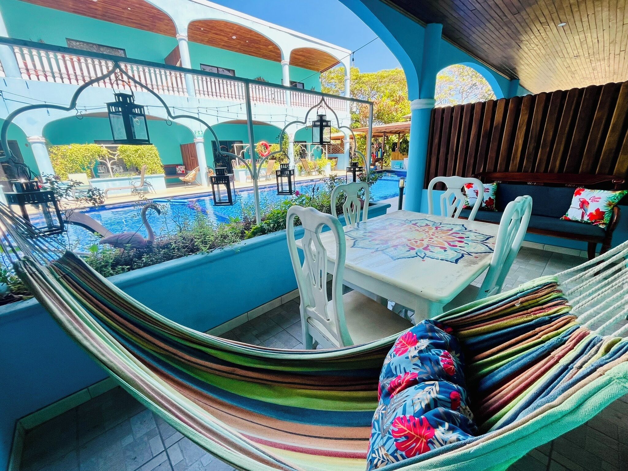 A hammock with a floral cushion, a pool, and a table with chairs in an outdoor setting.