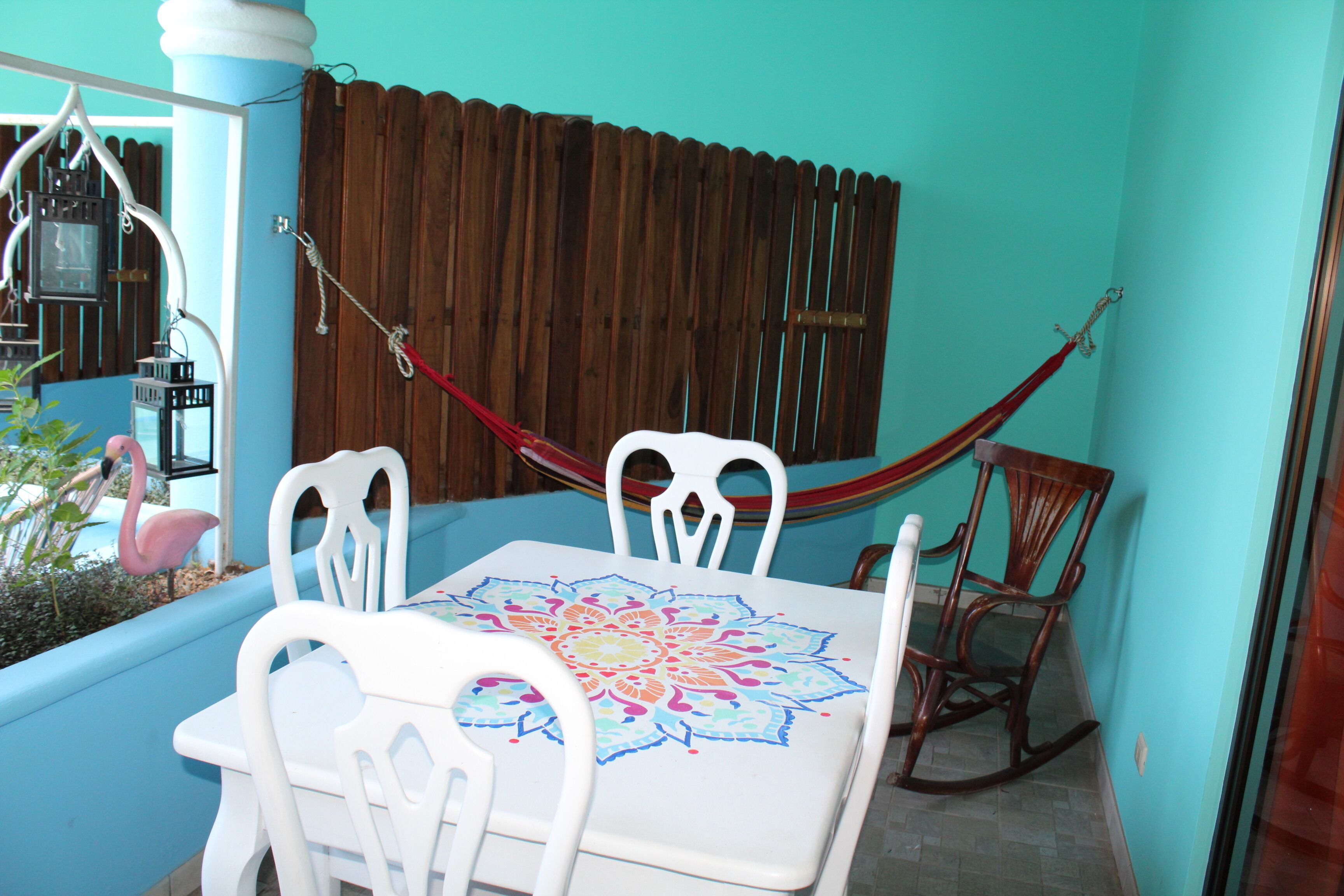 A dining area with a table and chairs, a hammock, and a wooden fence.