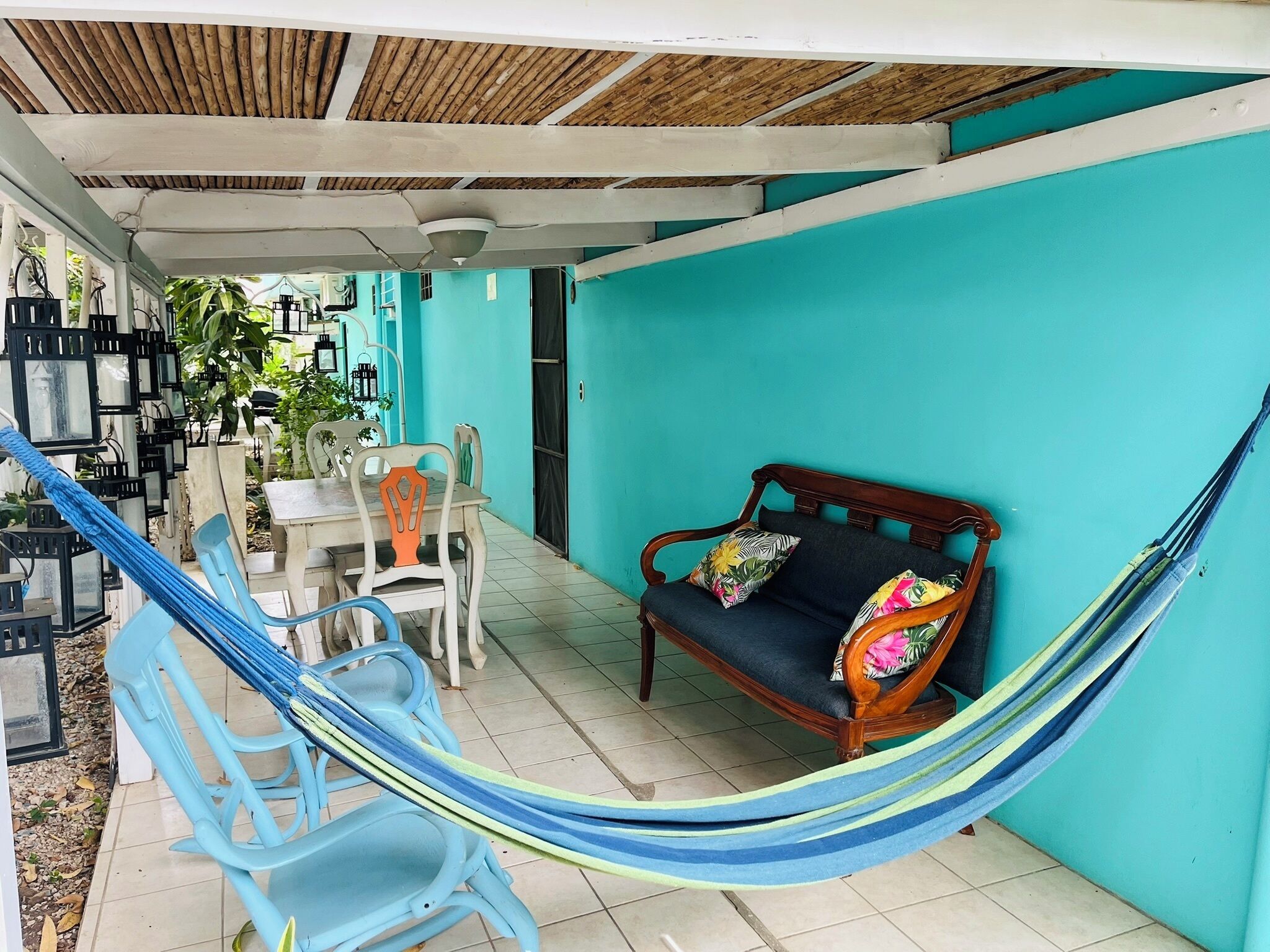 A covered outdoor seating area with a hammock, a table, chairs, and a sofa.