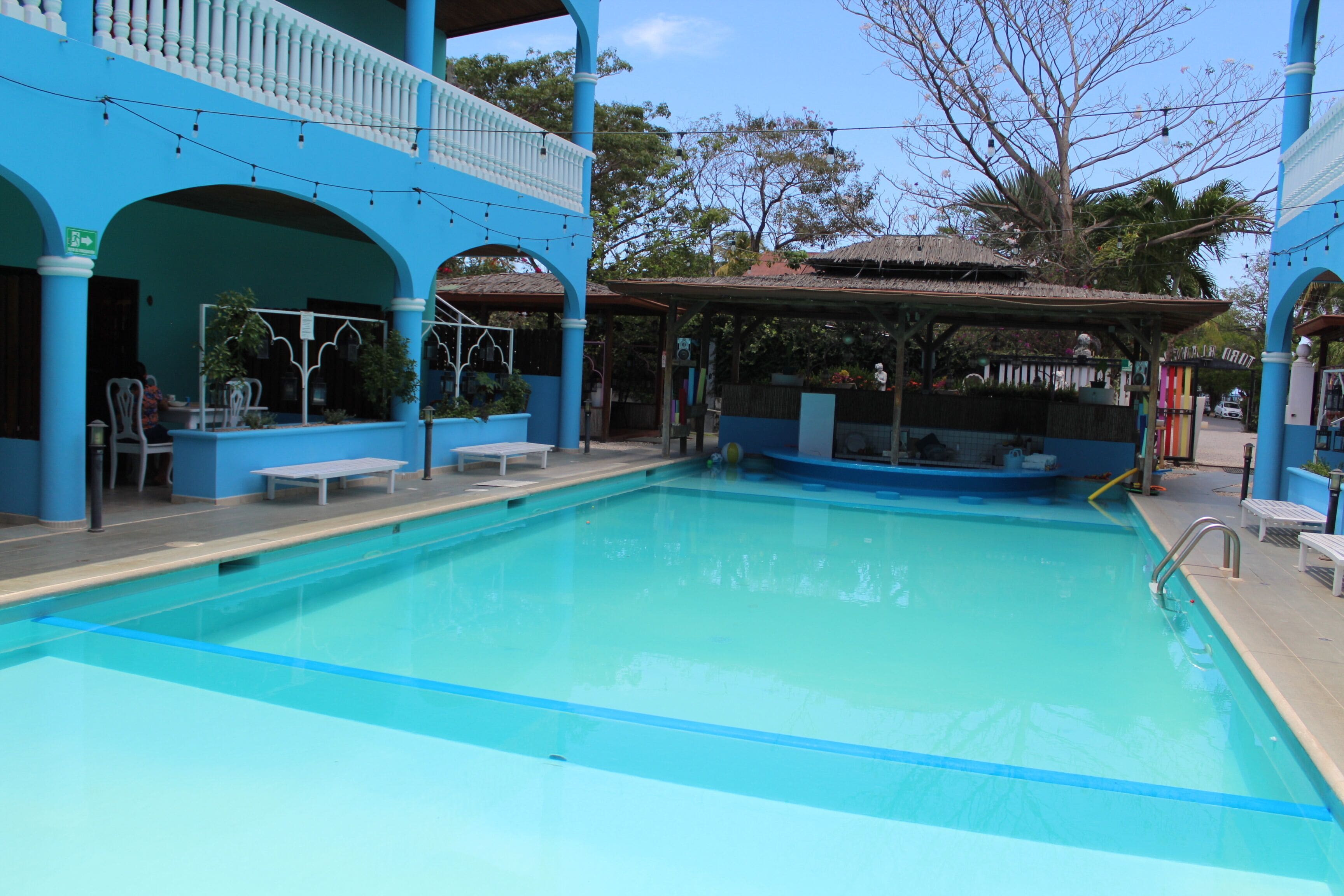 Una piscina con decoración azul y blanca, rodeada por una zona techada con bancos y plantas en macetas.