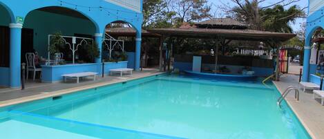 Una piscina con decoración azul y blanca, rodeada por una zona techada con bancos y plantas en macetas.