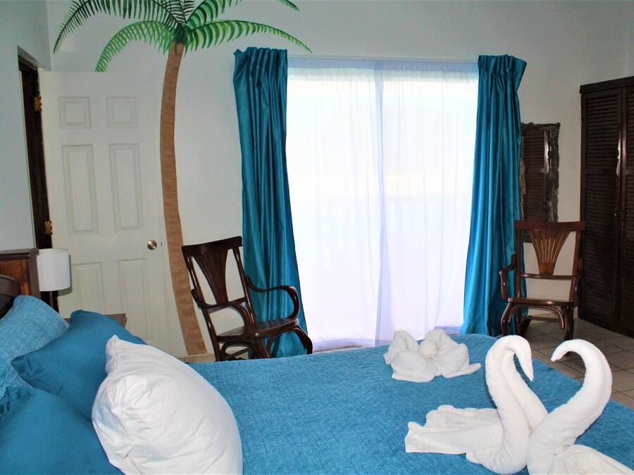 Habitació d'hotel amb un llit, dues cadires, un escriptori, una làmpada, una porta i una finestra amb cortines.