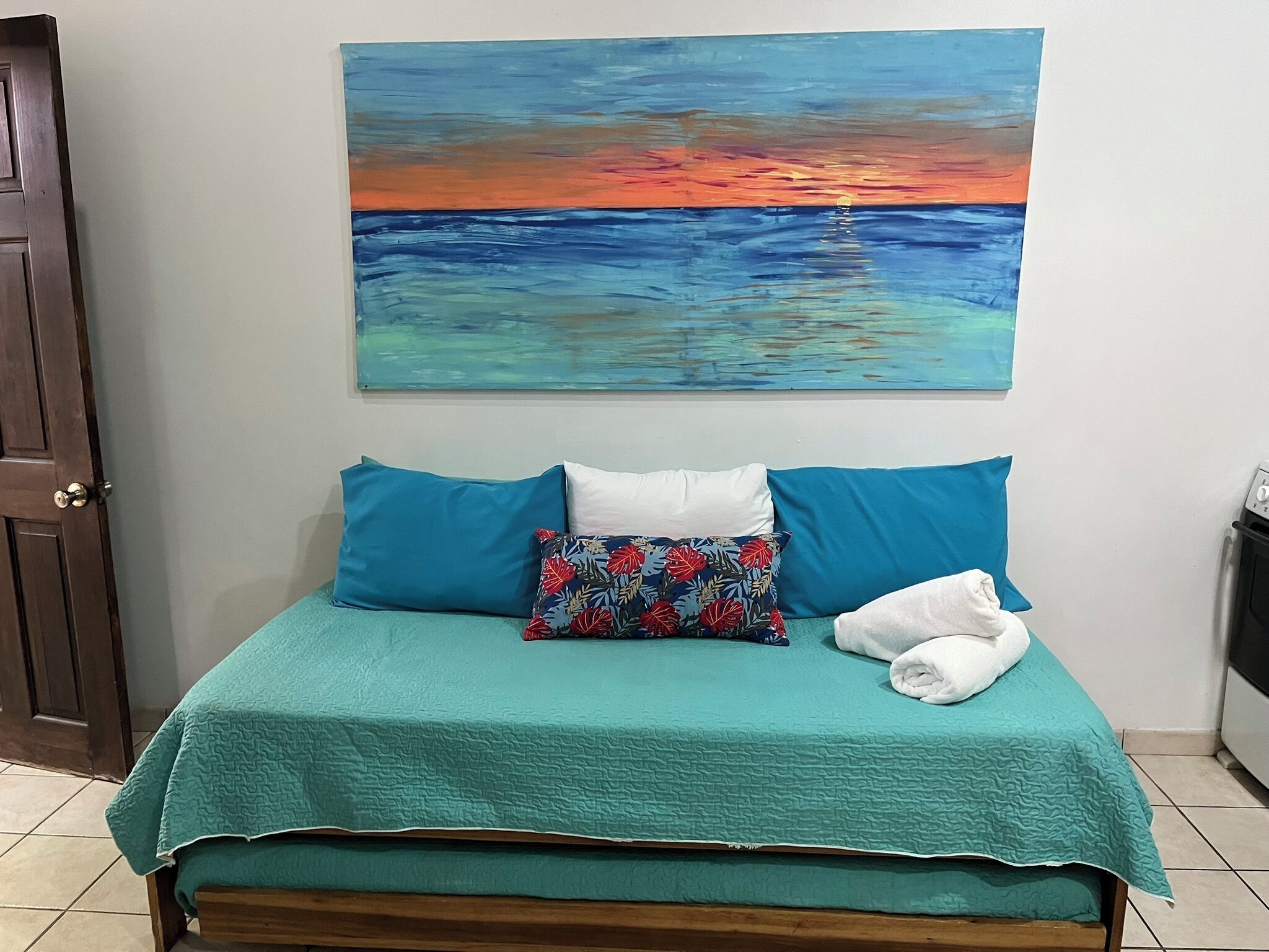 Una cama con una colcha color turquesa, dos almohadas y un cojín decorativo con estampado floral.