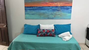 Una cama con una colcha color turquesa, dos almohadas y un cojín decorativo con estampado floral.