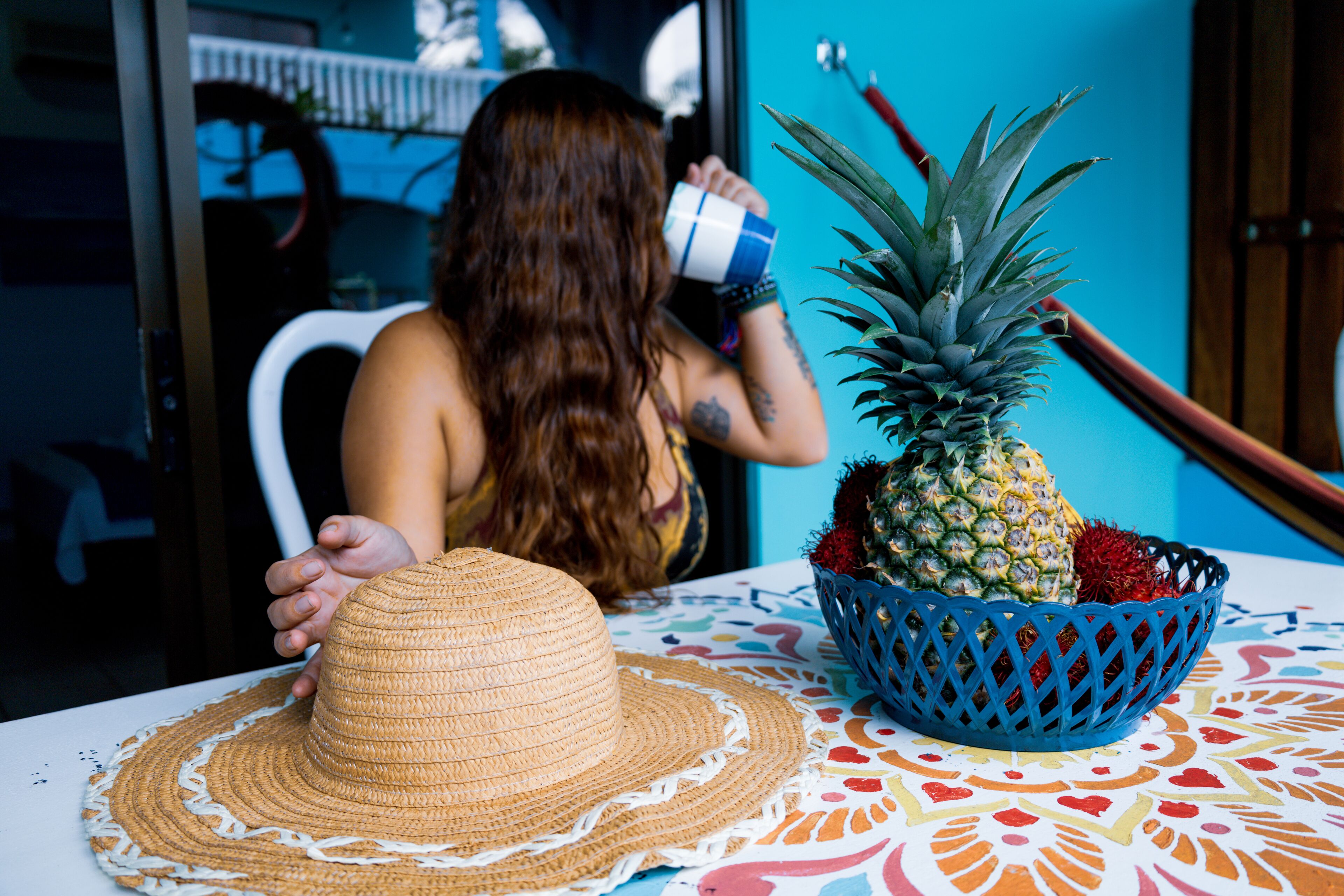 A person sitting at a table with a straw hat, a pineapple, and a blue basket.