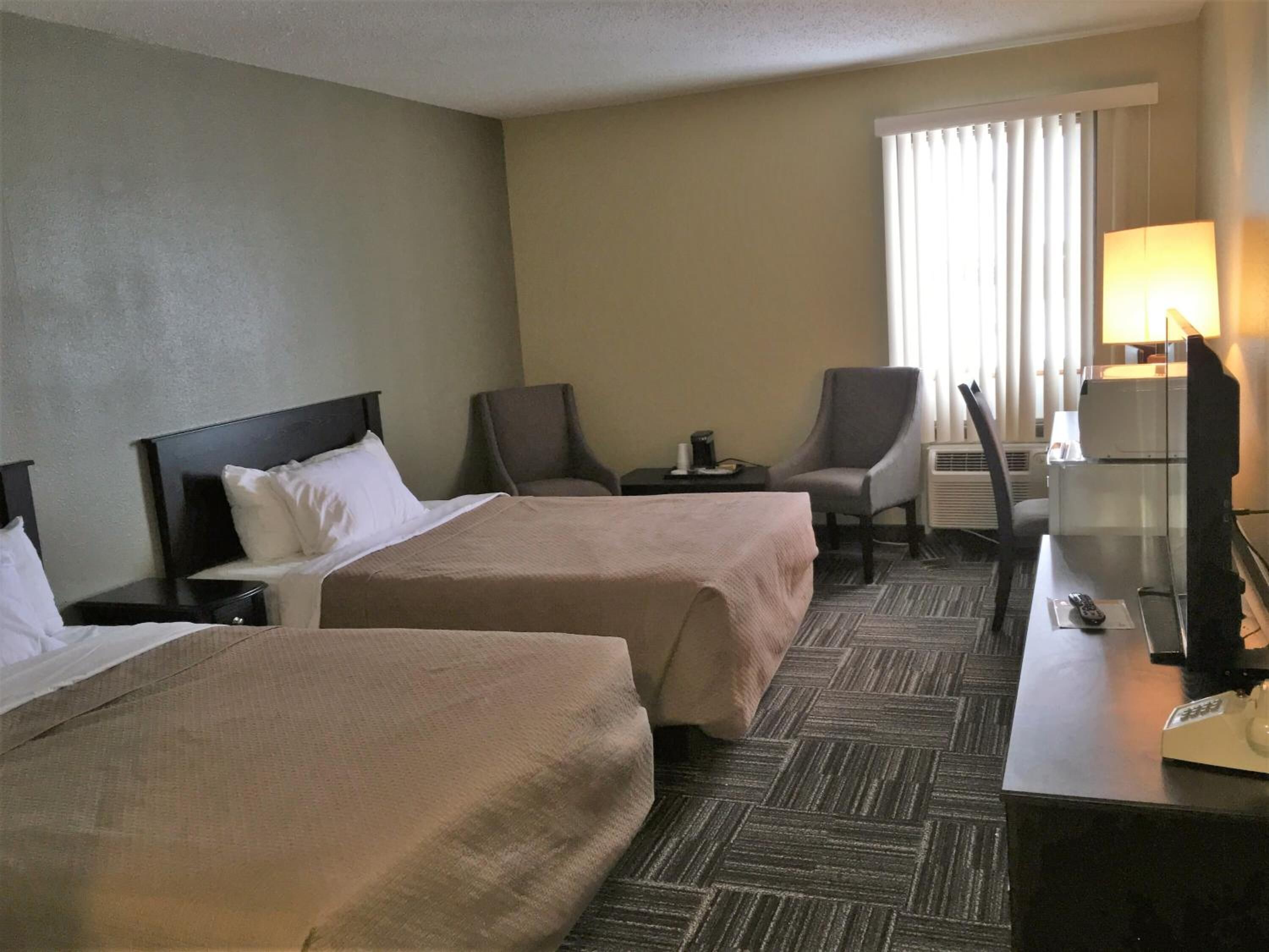 Una habitació d'hotel amb dos llits, un escriptori amb una làmpada, una cadira i una televisió.