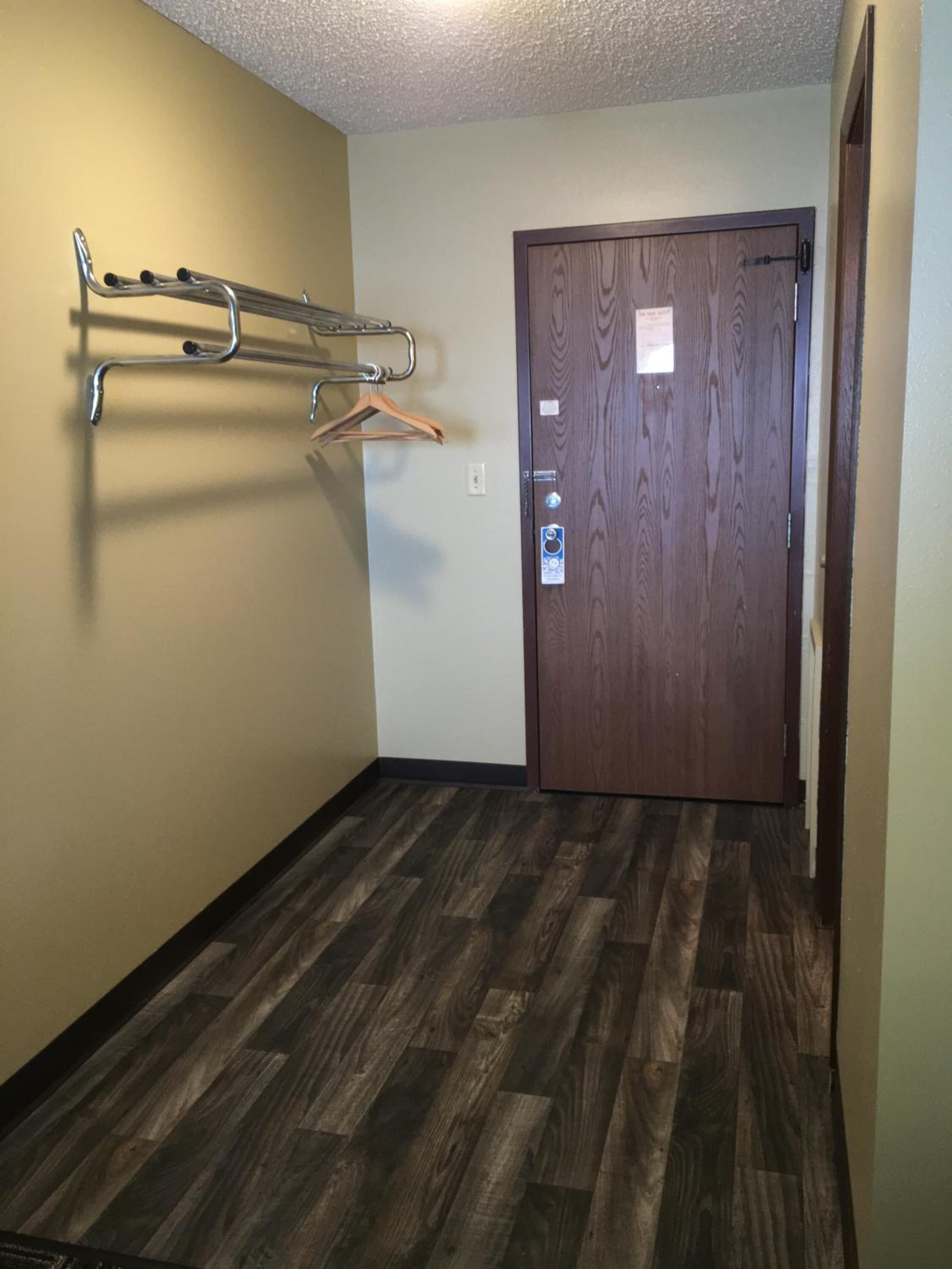 A hallway with a wooden door, a coat rack, and a textured floor.