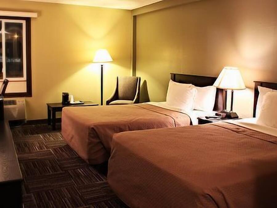 A hotel room with two beds, a desk, a chair, and two lamps.