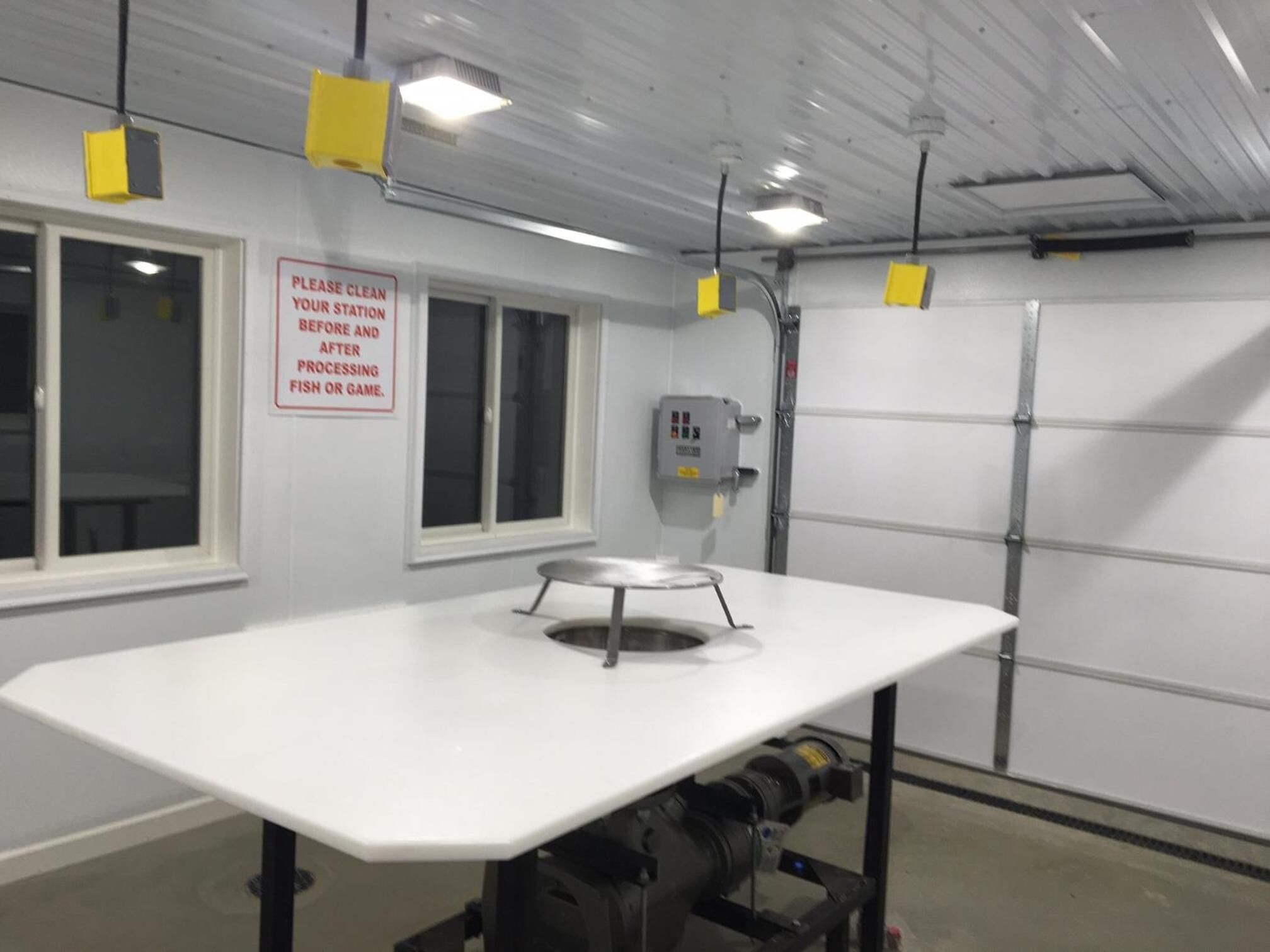 A clean, empty room with a white table, a window, and a sign instructing to clean the station before and after processing fish or game.