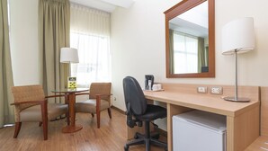 A hotel room with a wooden desk, two chairs, a small refrigerator, a lamp, a coffee maker, and a mirror. - Del Prado Hotel (Lima)