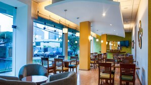 A restaurant with a modern interior, featuring a mix of round and rectangular tables, wooden chairs, and a large window offering a view of the street. - Del Prado Hotel (Lima)