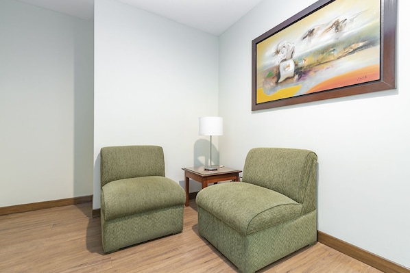A room with two green armchairs, a small wooden side table with a lamp, and a framed abstract painting on the wall. - Del Prado Hotel (Lima)