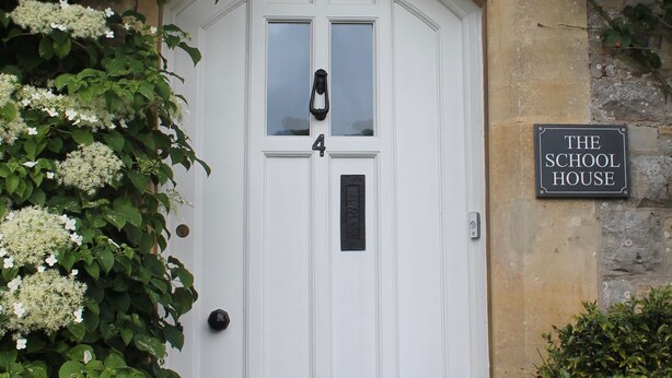 A white door with a black number plate, a black sign above it, and a stone wall. - The School House (Bridgwater)