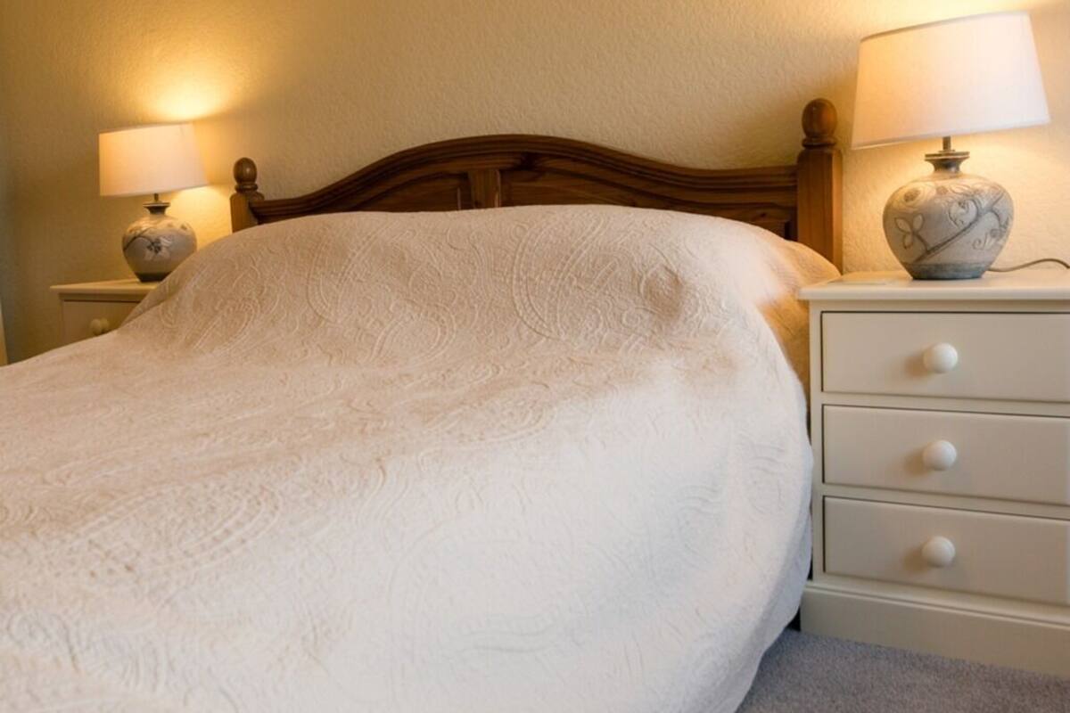 A neatly made bed with a white bedspread and two bedside lamps on white nightstands.