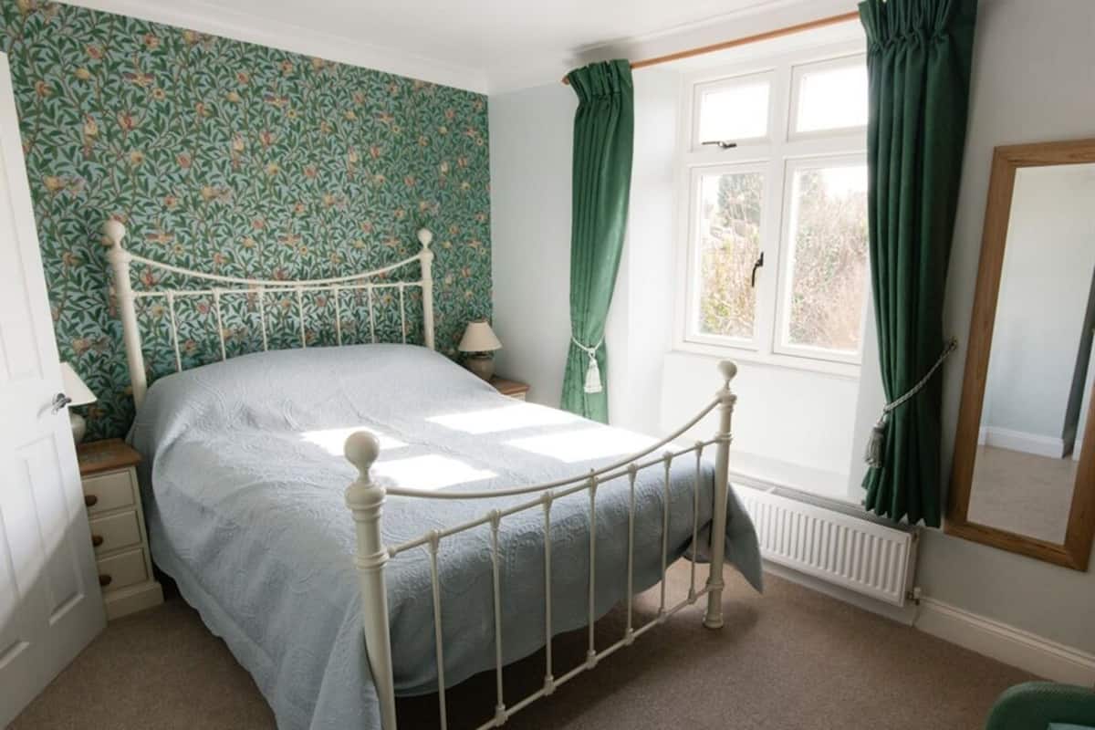 A bedroom with a bed, a window with curtains, a radiator, and a mirror.