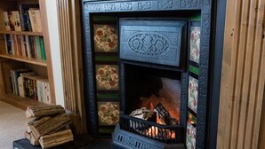 A fireplace with a fire, surrounded by bookshelves and a patterned rug. - The School House (Bridgwater)