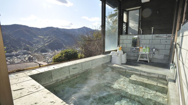 A hot tub with a mountain view, a glass door, and a tiled wall with toiletries. - Hotel Chobo Sanso (Yugawara)