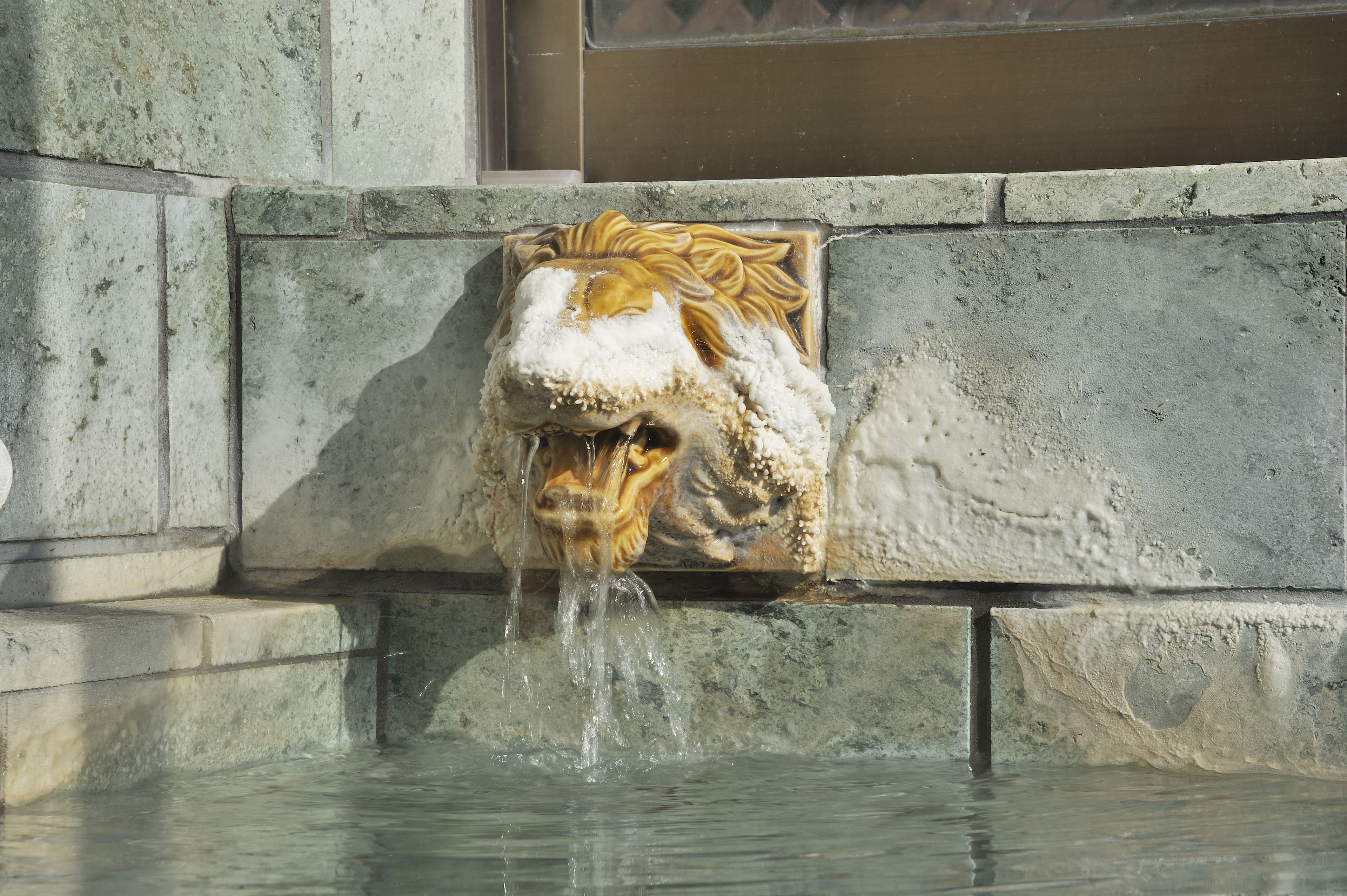 Una fuente de piedra con una escultura de cabeza de león y agua brotando de su boca.