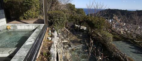 Un’onsen tradizionale giapponese con vasche in pietra, immerso in un paesaggio naturale e con vista sul mare.