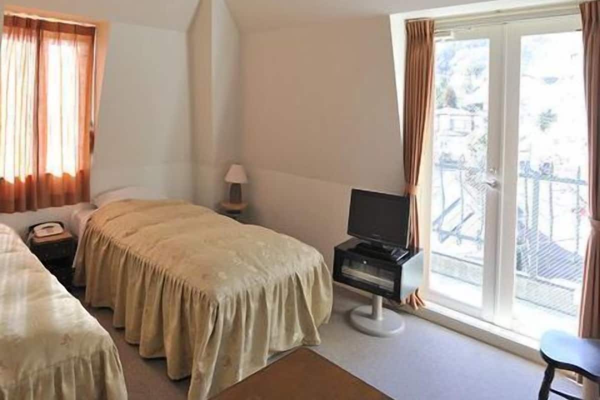 A hotel room with two beds, a desk with a computer, a lamp, and a large window with curtains.