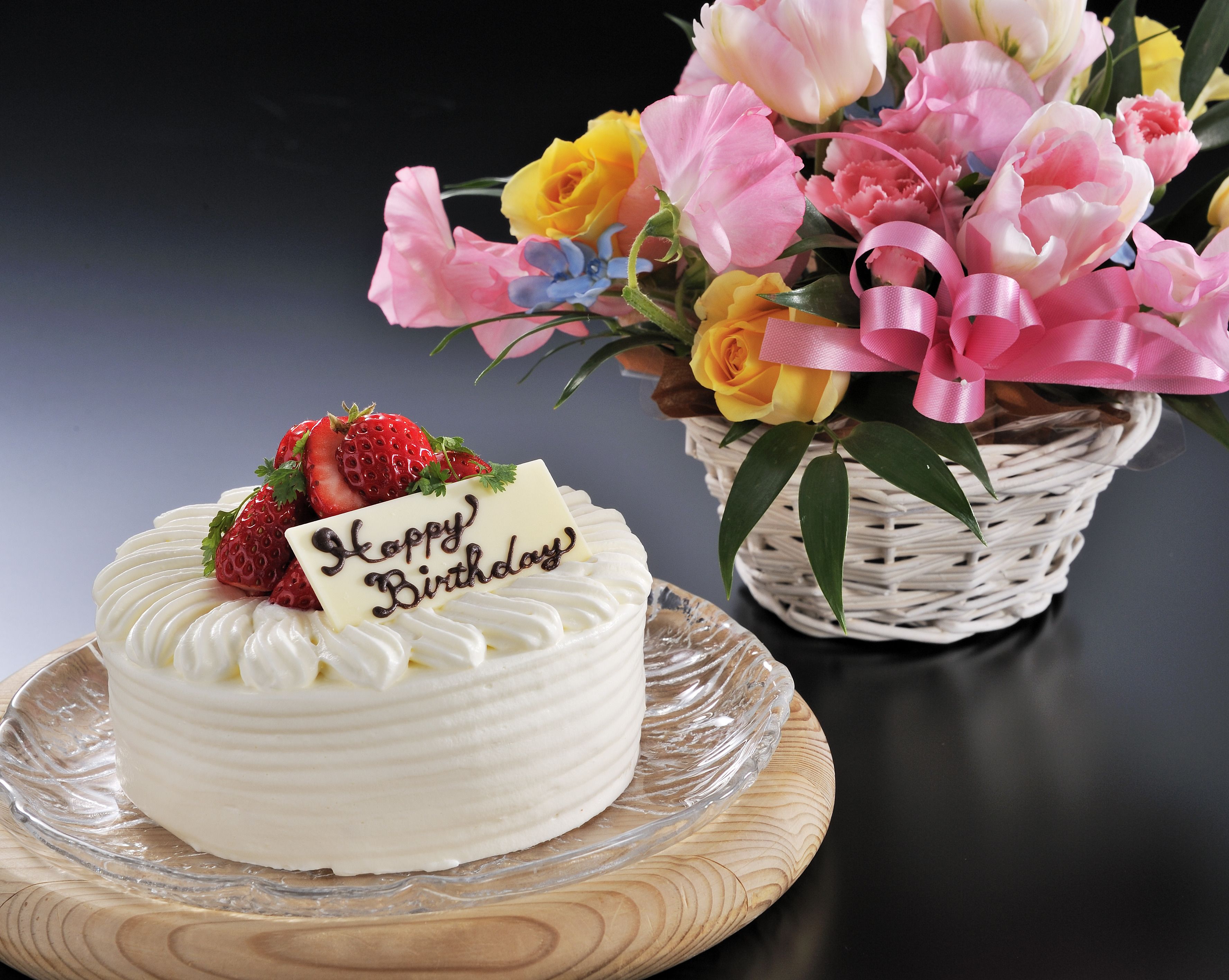 Un gâteau blanc, surmonté de fraises et décoré d’une inscription « Joyeux anniversaire », est posé sur une assiette en verre.