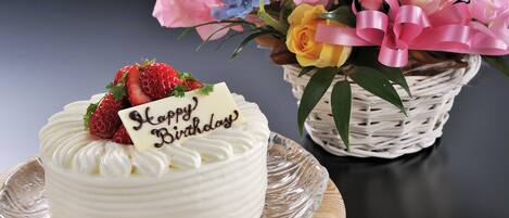 Un gâteau blanc, surmonté de fraises et décoré d’une inscription « Joyeux anniversaire », est posé sur une assiette en verre.